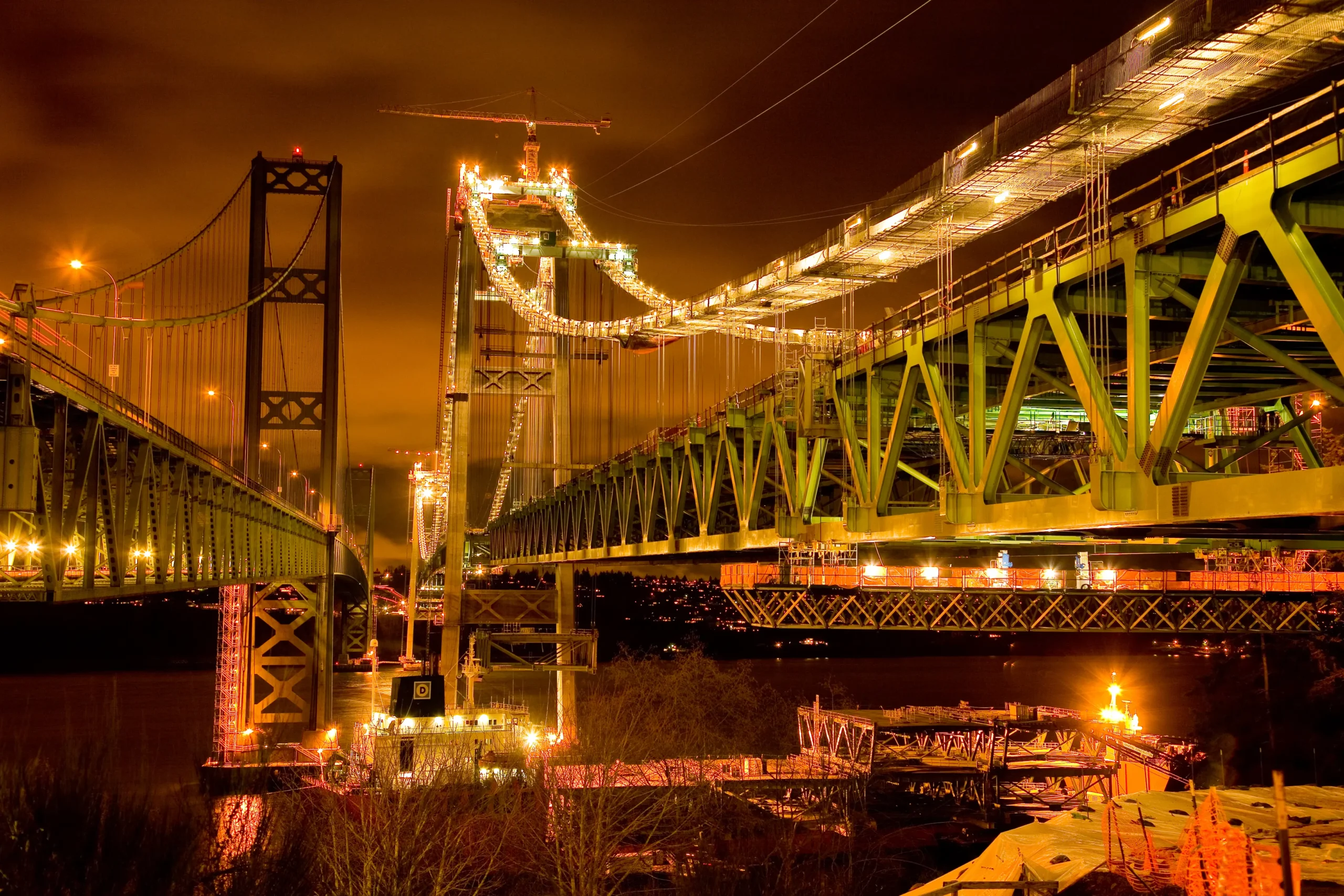 The new and existing Tacoma Narrows Bridges seen from Gig Harbor against a snowy sky.