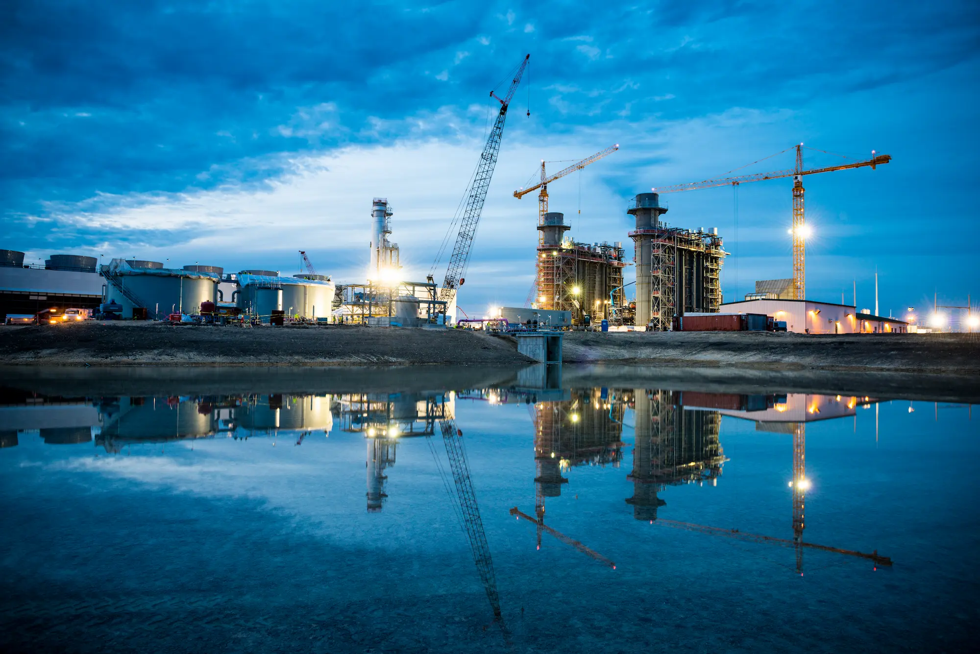 Panda Temple I Night view of the construction site with a raw water pond in the foreground, tower cranes and smokestacks in the background.