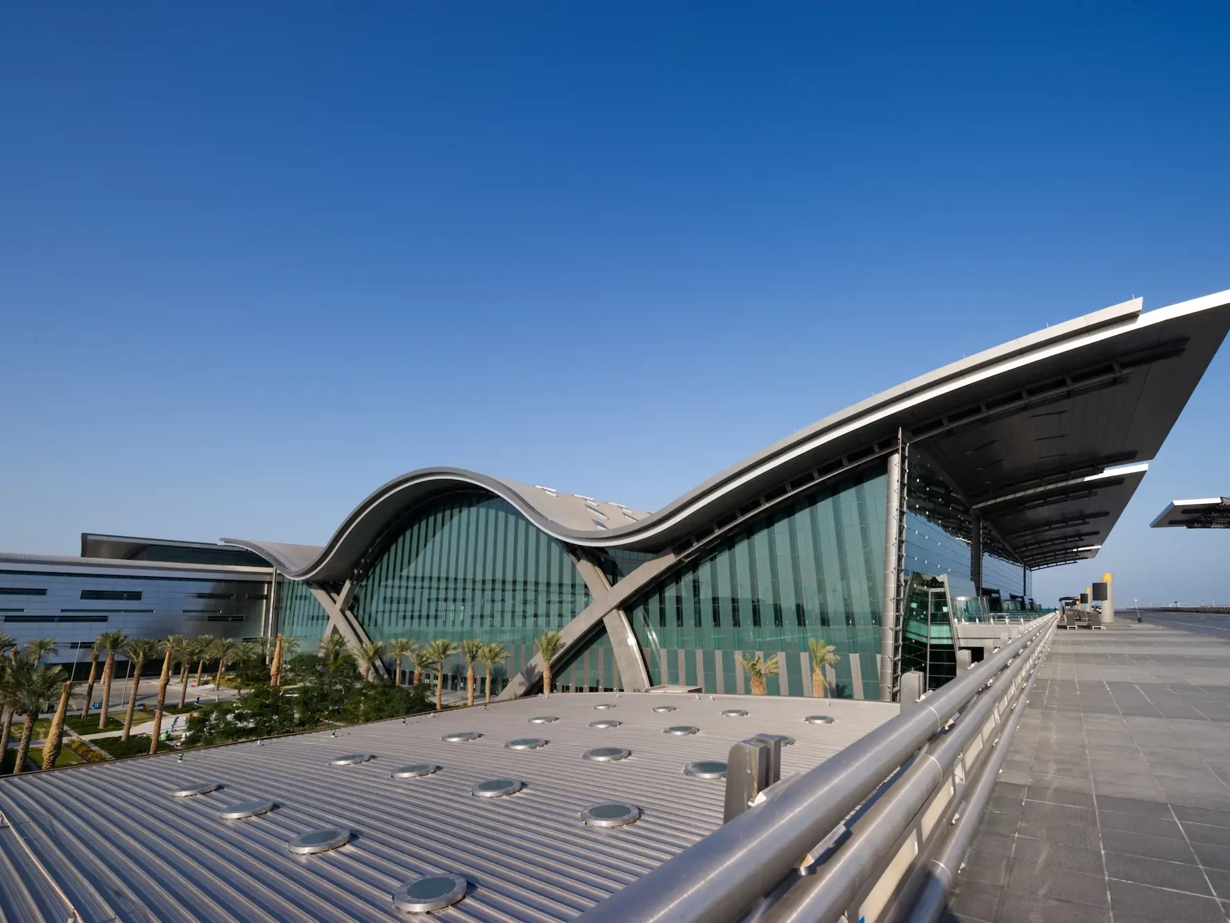 Exterior view of a modern airport with glass window walls and a wave shaped roof