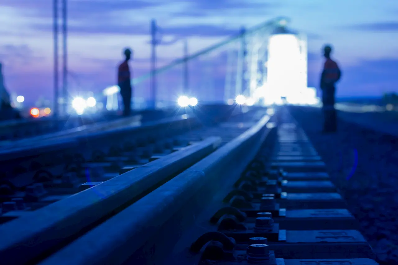 Night photo of the rail loop and train load out facilities. The plant is lighted against a dark blue sky. A man is silhouetted.