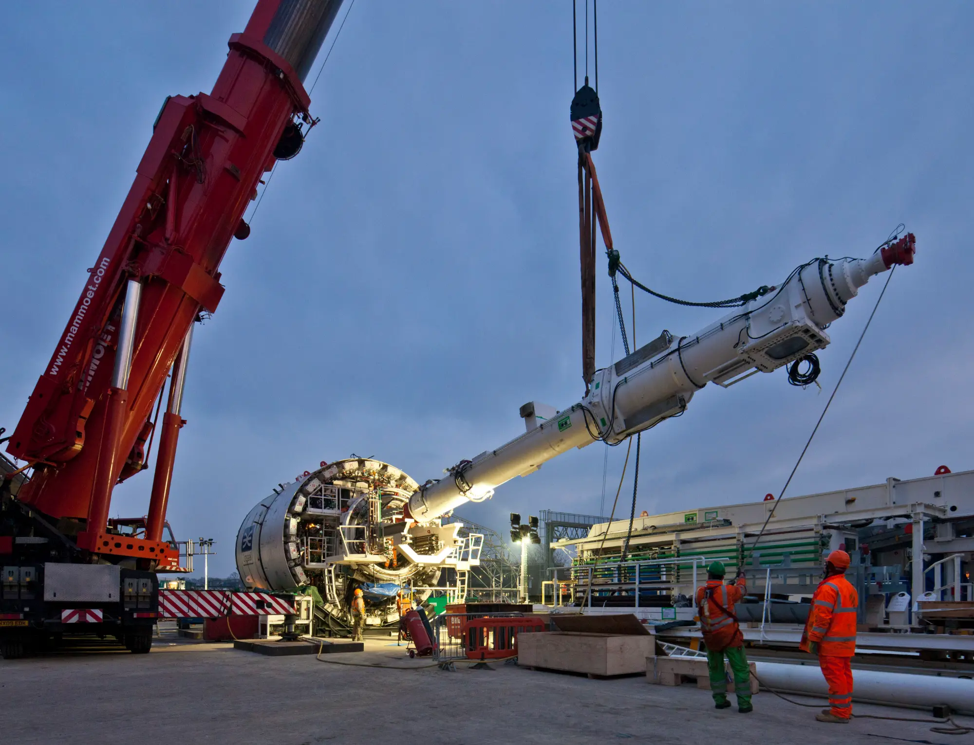 A part (shaft) is lifted (suspended) by a red crane.