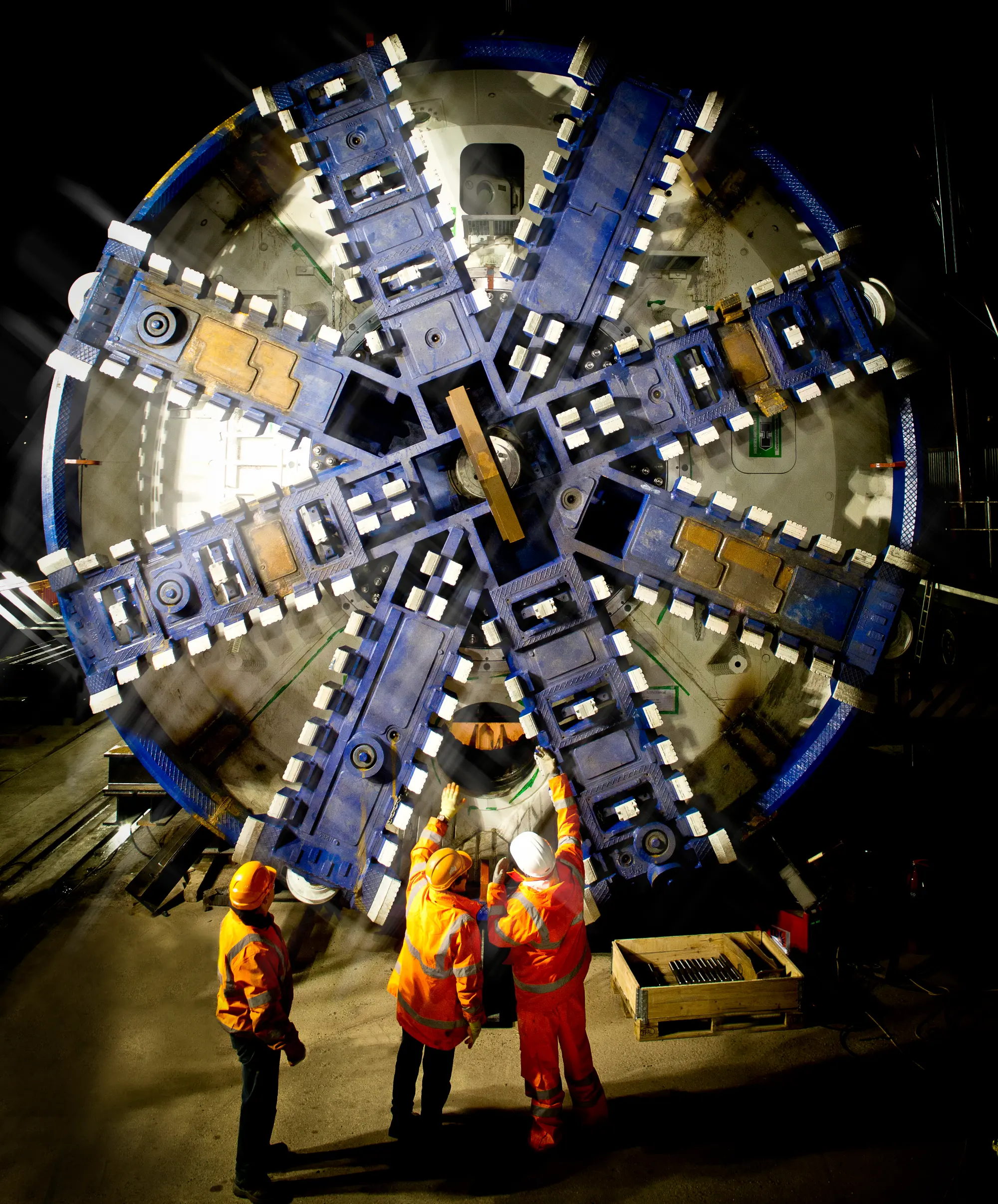The cutter head (rotating cutting wheel, drill) is installed at night. Workers (craftsmen) in the foreground point at the cutter head.