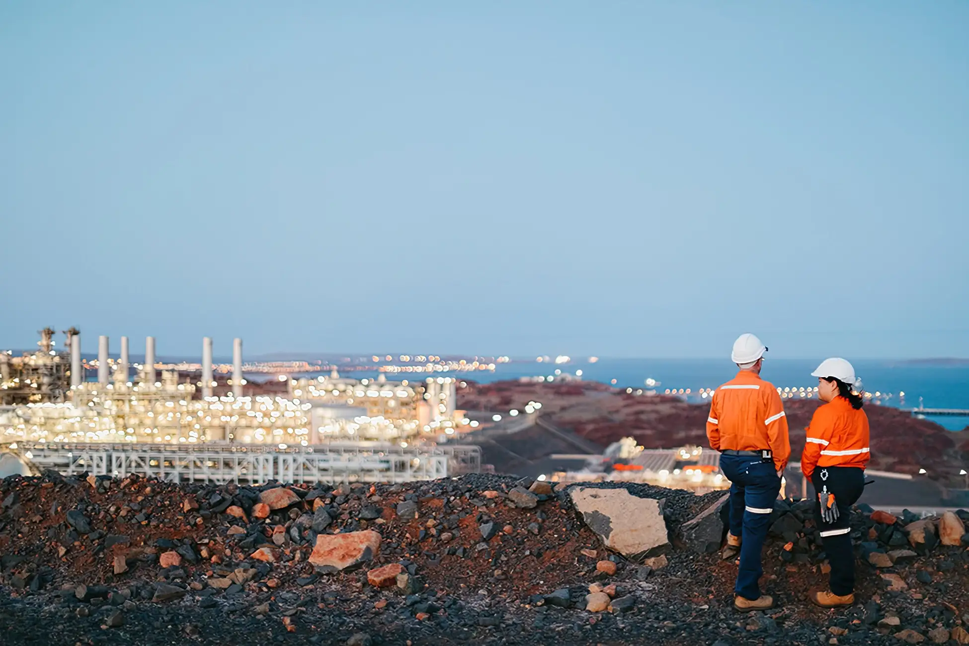 Workers stand overlooking the Pluto Train 2 jobsite at dusk.