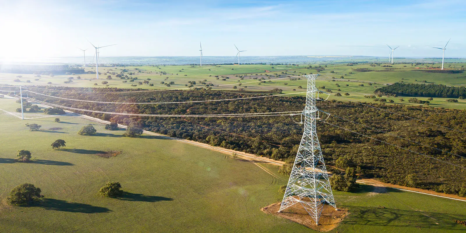 Image of energy transmission tower from above with green fields and the ocean in the distance.